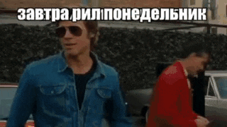 a man wearing sunglasses and a denim jacket is standing in front of a car and talking in a foreign language .