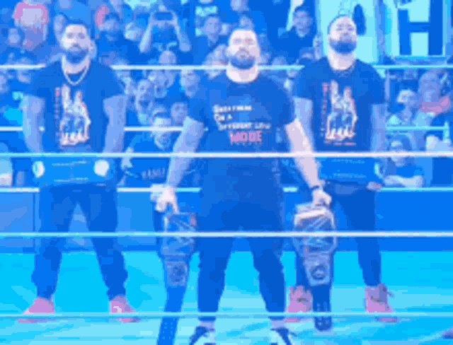 three men are standing in a wrestling ring holding championship belts
