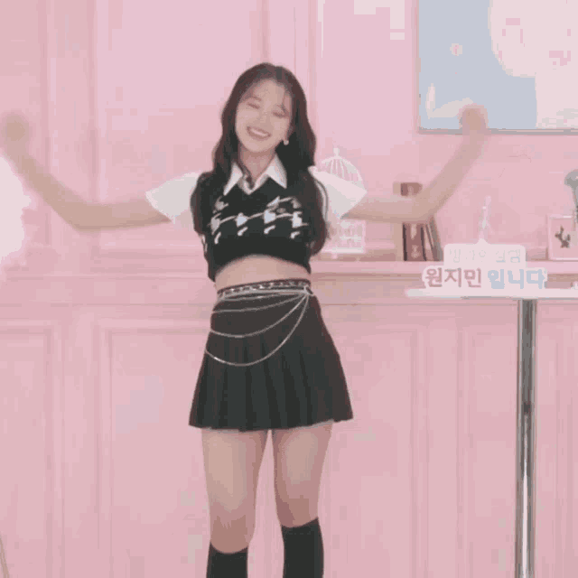 a girl in a black skirt is dancing in front of a pink wall with a sign in a foreign language