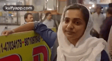 a woman in a white scarf is leaning on a yellow sign in a crowded area .
