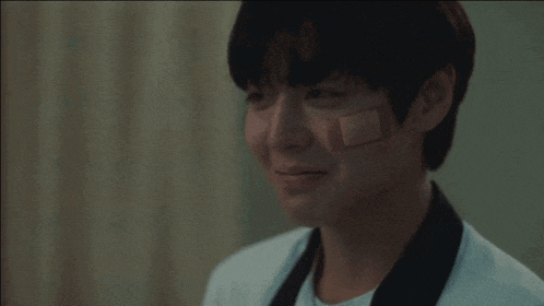 a young boy in a hospital gown with a bandage on his forehead .