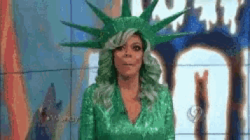 a woman in a green dress and a statue of liberty hat is standing in front of a screen .