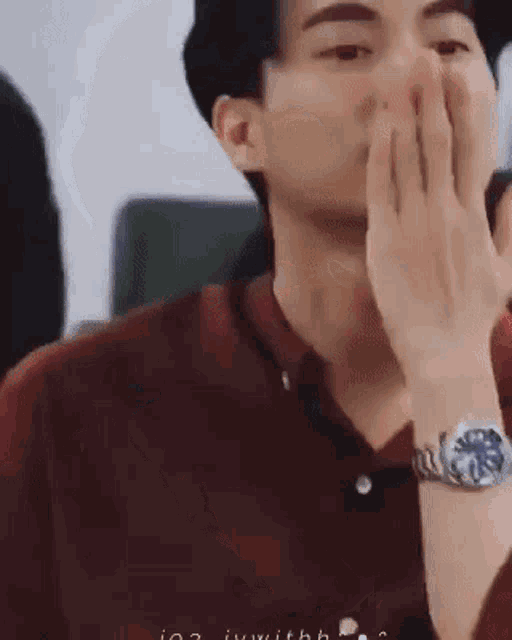 a man wearing a watch is covering his face with his hand .