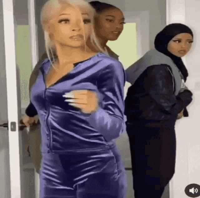 three women are standing next to each other in a room . one of the women is wearing a purple tracksuit .