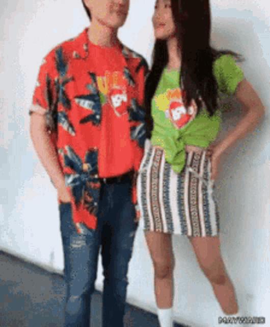 a man in a red shirt and a woman in a green shirt are standing next to each other and looking at each other