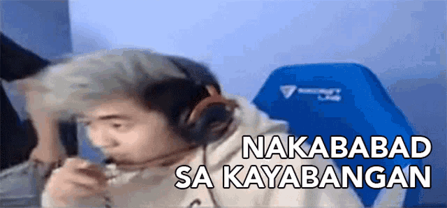 a man wearing headphones is sitting in a blue chair with the words nakababad sa kayabangan above him