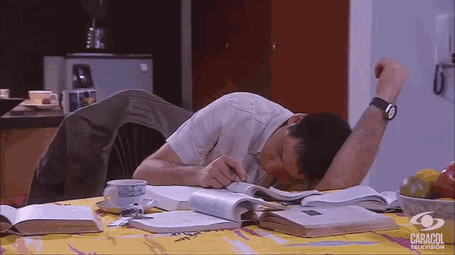 a man is sleeping on a table with books and a caracol television logo in the corner