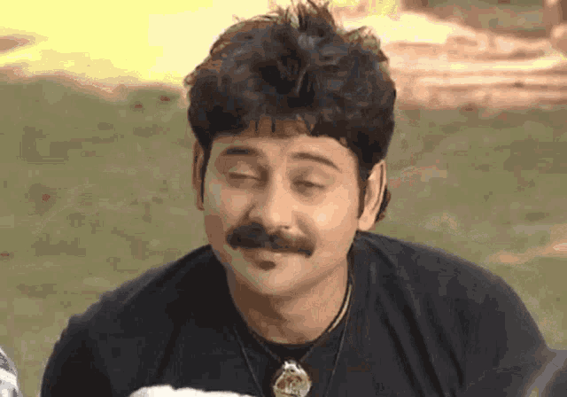a man with a mustache wearing a black shirt and necklace