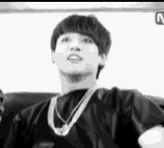 a black and white photo of a young man wearing a necklace and a t-shirt .