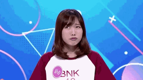 a young woman is making a funny face in front of a blue background while wearing a bnk shirt .