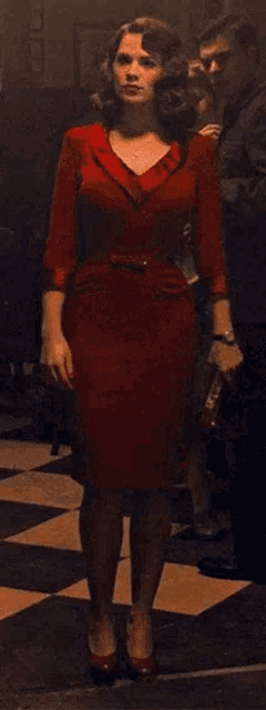 a woman in a red dress is standing on a checkerboard floor