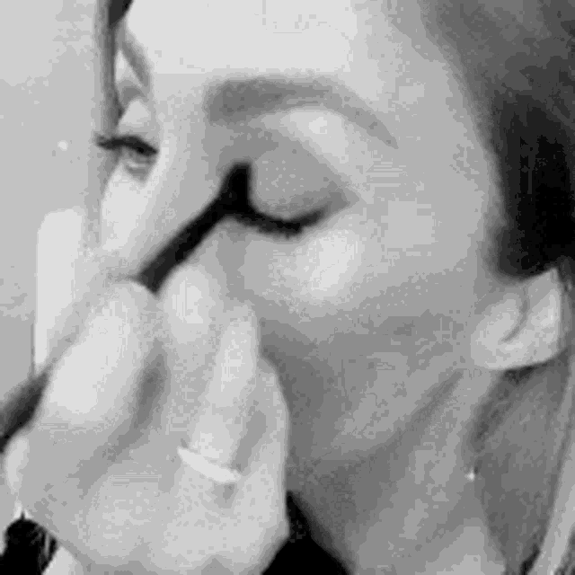 a black and white photo of a woman applying eyeliner to her eye .