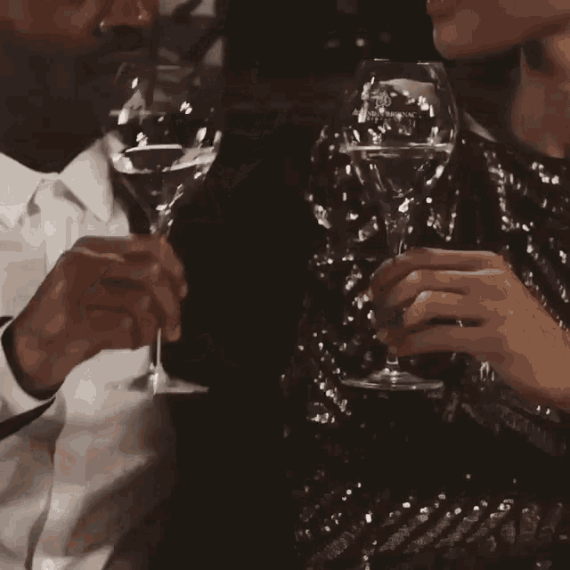 a man and a woman toasting with wine glasses with a crown on the glass