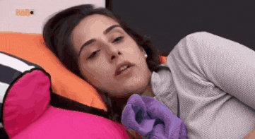 a woman is laying on a bed with a pink pillow and a purple glove .