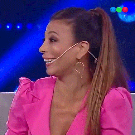 a woman wearing a pink top and gold hoop earrings is smiling while sitting in front of a microphone .