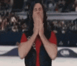 a man with long hair is covering his mouth with his hands while wearing a red shirt .
