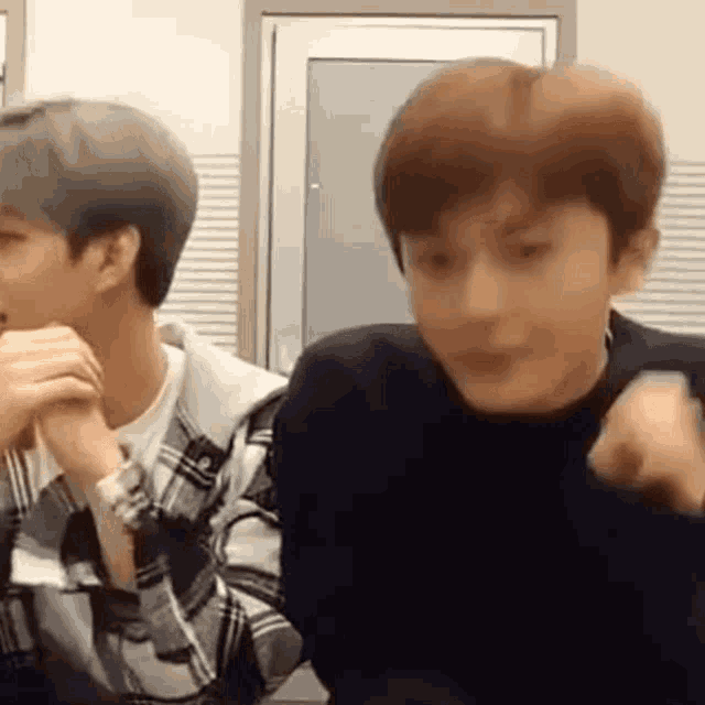 two young men are sitting next to each other in a room and talking .
