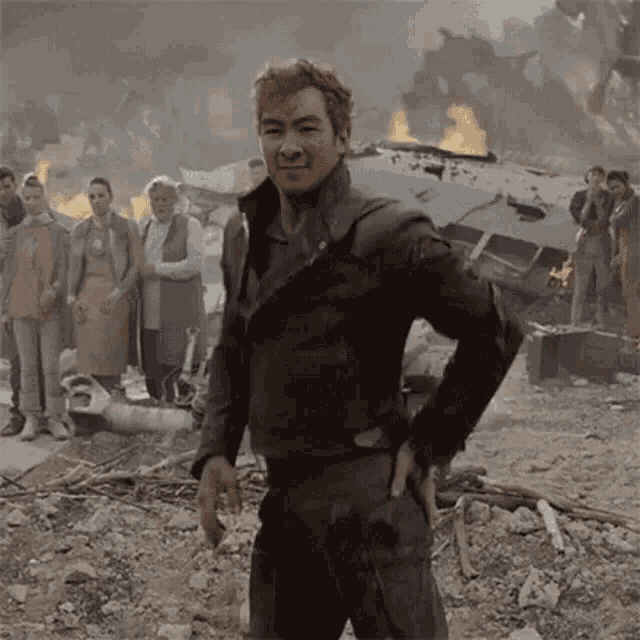 a man with his hands on his hips is standing in front of a group of people in a destroyed city .