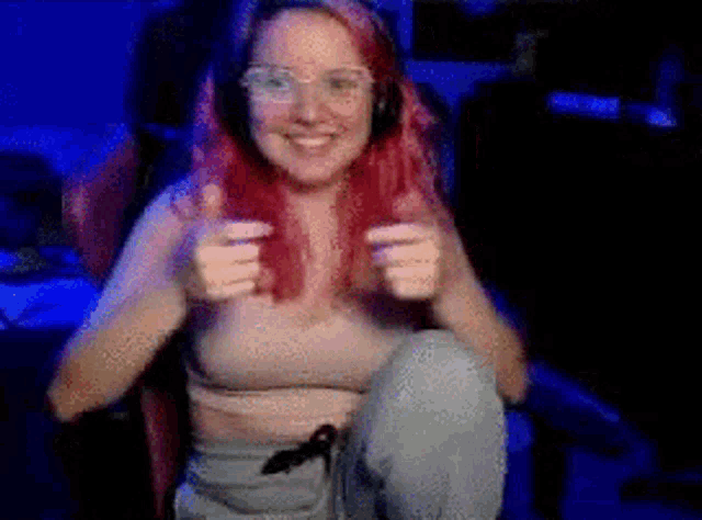 a woman with red hair and glasses is sitting in a chair and giving two thumbs up .