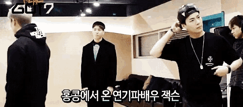a group of men are standing in a room with a sign that says got 7 on it .