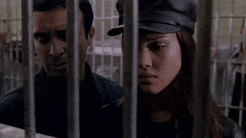 a police officer is standing next to a woman in a jail cell behind bars .