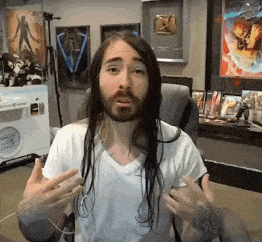 a man with long hair and a beard is wearing a white shirt and sitting in a chair .
