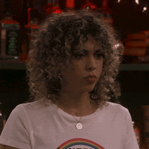 a woman with curly hair is wearing a rainbow t-shirt