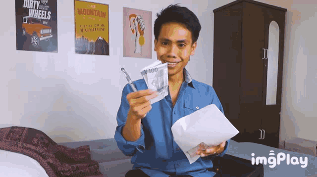a man holding a pen and a 100 dollar bill in front of dirty wheels posters on the wall
