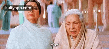two older women are sitting next to each other in a room and talking to each other .