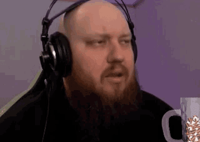 a bald man with a beard wearing headphones is sitting in front of a microphone .