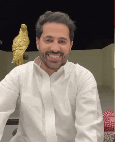 a man in a white shirt smiles in front of a gold parrot statue