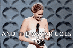 a woman in a white dress is holding an oscar statue in front of a microphone and the oscar goes to .