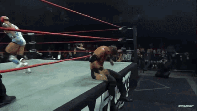 a wrestler is sitting on the edge of a wrestling ring with a subscribe button in the corner