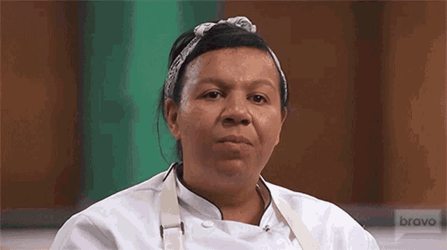 a woman in a chef 's uniform and apron is sitting in front of a green wall .