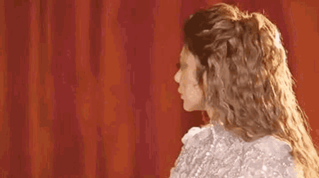 a woman with long curly hair is wearing a white dress .
