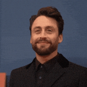 a man with a beard wearing a suit and black shirt smiles for the camera