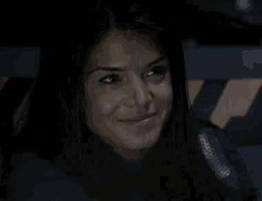 a woman is smiling in a dark room and looking at the camera .