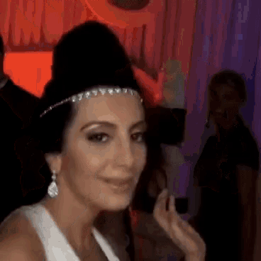 a woman in a white dress and a black hat is smiling while standing in a dark room .