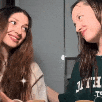 two young women are sitting next to each other at a table and smiling .
