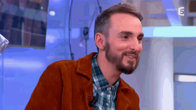 a man with a beard and a plaid shirt is smiling in front of a screen that says direct 5