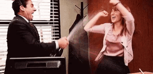 a man and a woman are standing next to each other in an office and laughing .
