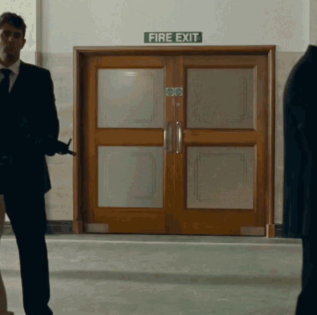 a man in a suit and tie stands in front of a fire exit