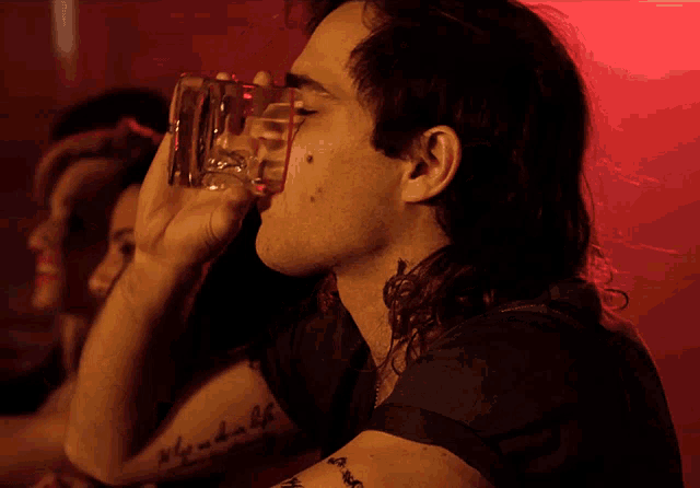 a man drinking from a glass with a tattoo on his arm that says why and how of life