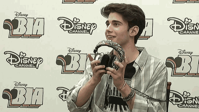 a man is holding a pair of headphones in front of a wall with disney channel logos