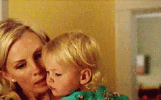 a woman is holding a little girl in her arms and kissing her on the forehead .