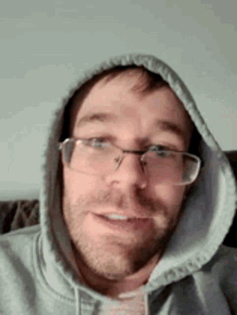 a man wearing glasses and a hoodie is smiling and looking at the camera .