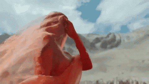 a woman in a red dress is standing in front of a mountain covered in a veil .
