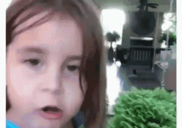 a little girl is making a funny face in front of a green plant in a living room .