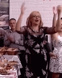 a woman in a black dress is standing in front of a table with her hands in the air .
