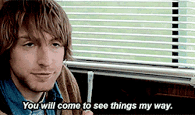 a man is sitting in front of a window with blinds and says " you will come to see things my way "